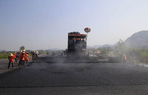 2019年8月，宜春經(jīng)開區(qū)S311路面攤鋪現(xiàn)場(chǎng)，工友們輔助路面兩側(cè)的分料、補(bǔ)窩等作業(yè)